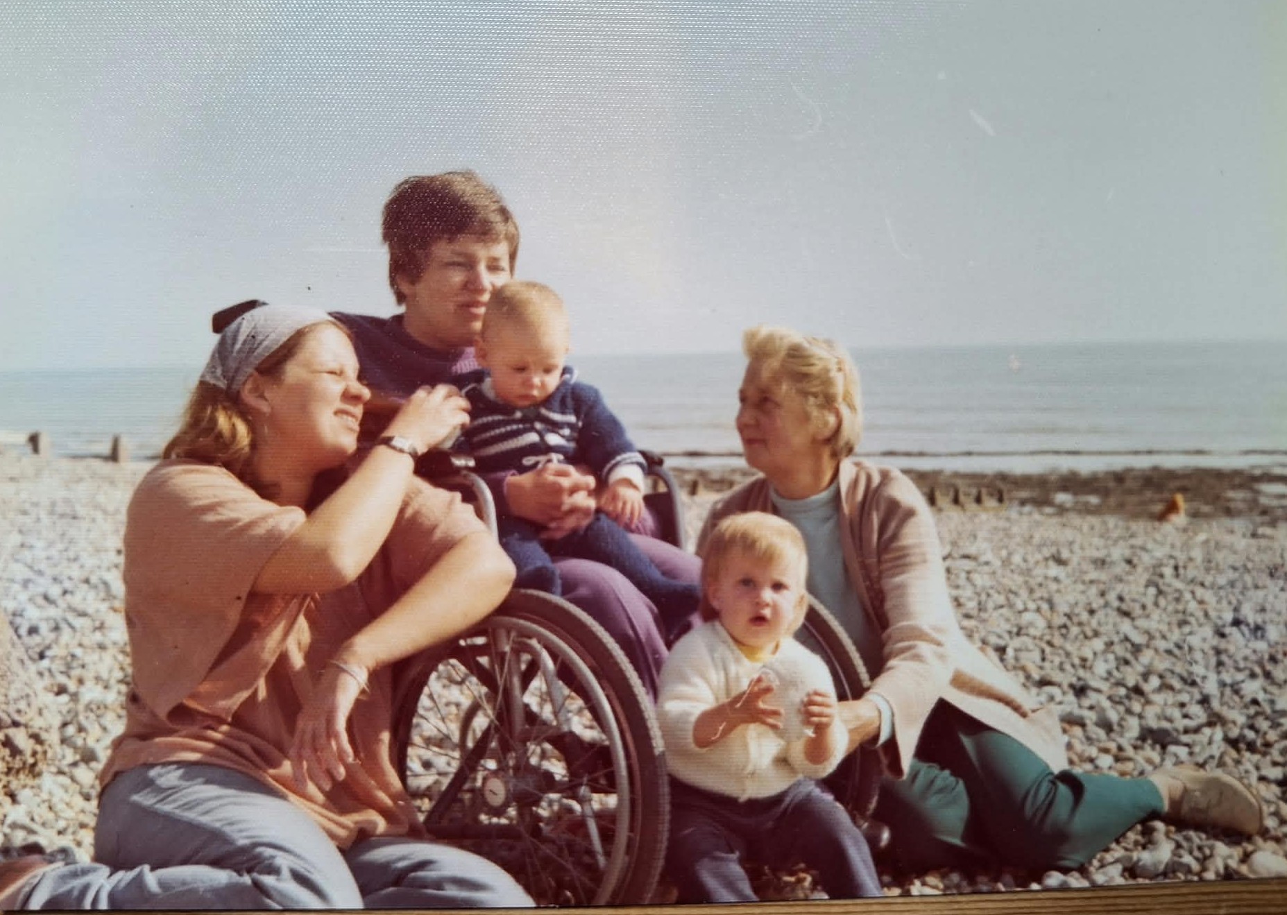 A family together on a pebble beach, including a wheelchair user and two young children